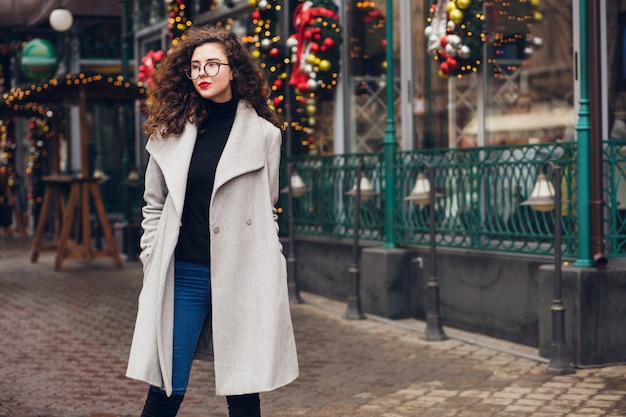 Jovem mulher elegante andando na rua com casaco cinza outono, cabelo encaracolado, frio, tendência da moda estilo casual