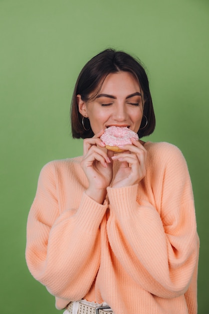 Foto grátis jovem mulher elegante com um suéter casual cor de pêssego isolado em uma parede verde-oliva com rosquinha rosa e espaço para cópia