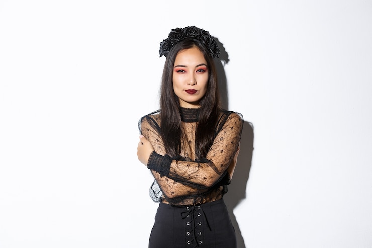 Foto grátis jovem mulher elegante em um elegante vestido gótico e grinalda, abraçando o corpo dela e olhando atrevida para a câmera, vestindo a fantasia de halloween da viúva morta-viva, em pé sobre um fundo branco.