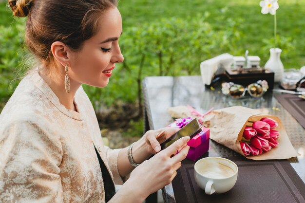 Jovem mulher elegante sentada em um café, segurando um telefone inteligente