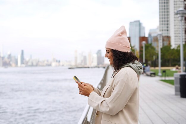 Jovem mulher elegante usando smartphone ao ar livre enquanto explora a cidade