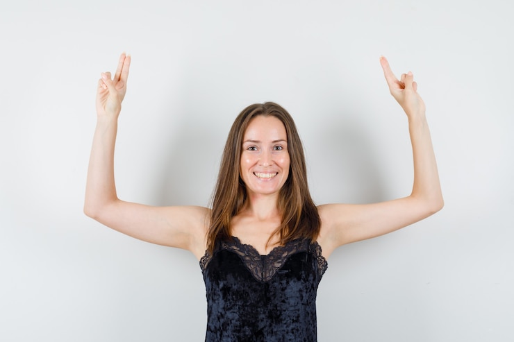 Foto grátis jovem mulher em camiseta preta levantando os braços com dois dedos e parecendo alegre