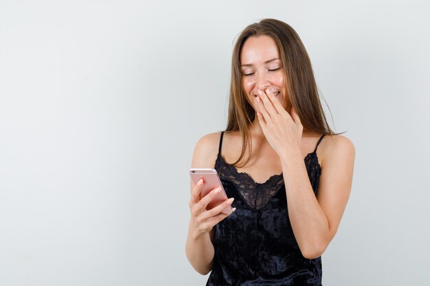 Jovem mulher em camiseta preta olhando para o celular e parecendo feliz