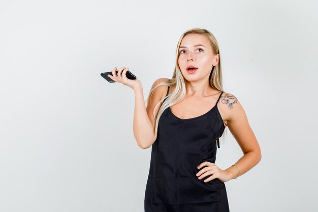 Jovem mulher em camiseta preta posando, segurando um smartphone e parecendo encantadora