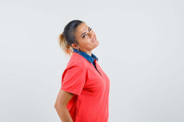 Jovem mulher em pé, olhando por cima do ombro e posando com uma camiseta vermelha e parecendo irritada. vista frontal.
