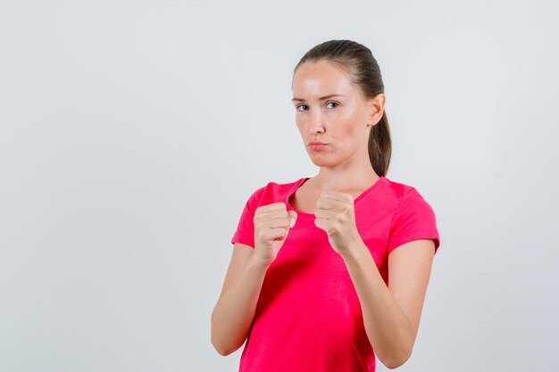 Jovem mulher em pose de boxeador em t-shirt rosa e olhando sério. vista frontal.