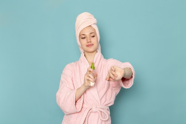 jovem mulher em roupão rosa usando spray corporal em azul