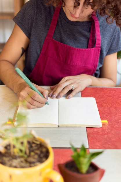 Jovem mulher escrevendo algo no caderno ao lado de plantas