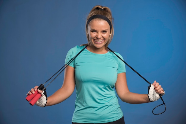 Jovem mulher esportiva pendurando cordas de pular em seu pescoço e sorrindo.