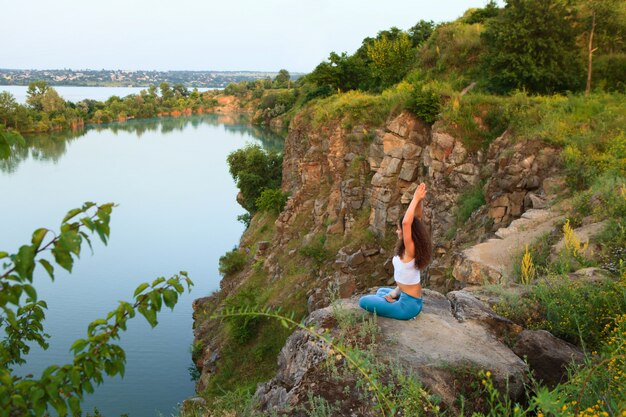 Jovem mulher está praticando ioga perto do rio