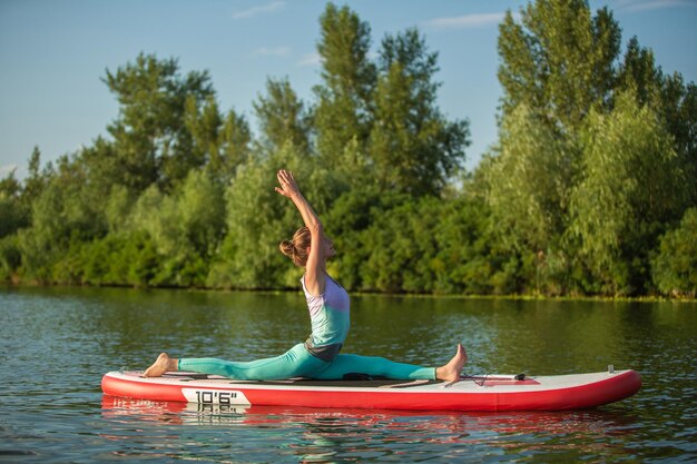 Jovem mulher fazendo ioga a bordo de sup com remo. Pose meditativa, vista lateral - conceito de harmonia com a natureza, vida livre e saudável, freelance, negócios remotos.