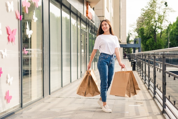 Jovem mulher feliz com sacolas de compras, andando na rua.