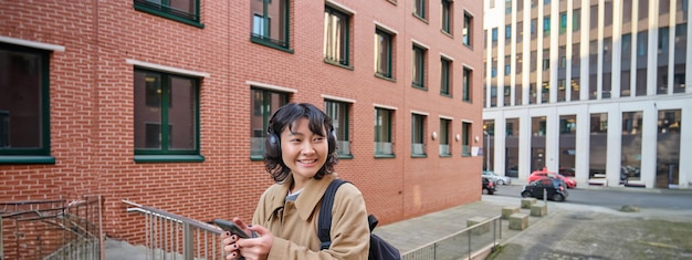 Jovem mulher feliz com sobretudo ouve música em fones de ouvido segura smartphone usa celular