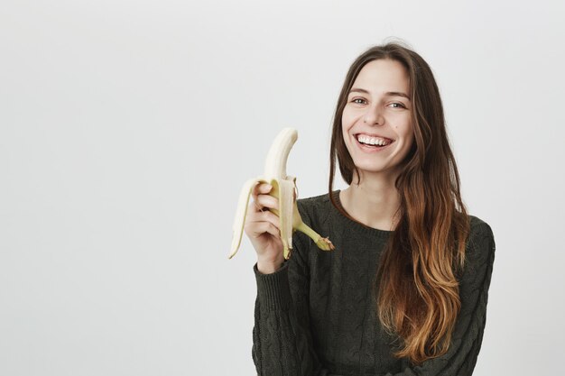 Jovem mulher feliz comendo banana e rindo