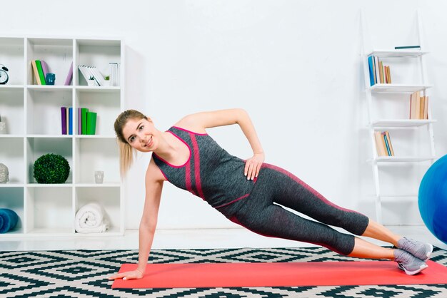 Jovem mulher feliz da aptidão que veste o sportswear que faz o exercício na sala de visitas