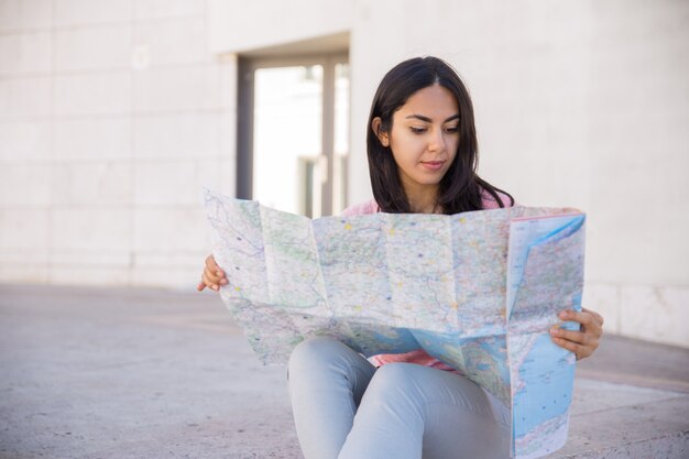 Jovem mulher focalizada que estuda o mapa de papel ao ar livre