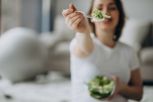 Jovem mulher grávida comendo salada em casa