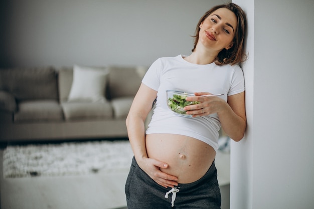 Jovem mulher grávida comendo salada em casa