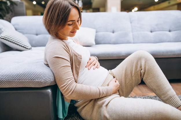 Jovem mulher grávida em casa pelo sofá segurando a barriga