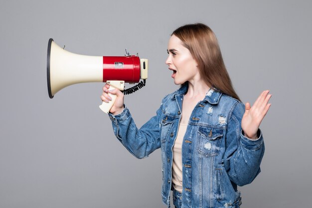 Jovem mulher gritando no megafone com parede cinza de braço isolado