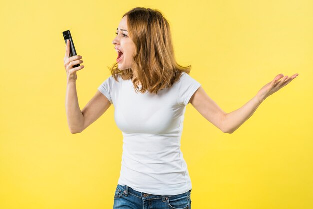 Jovem mulher gritando no telefone inteligente contra fundo amarelo