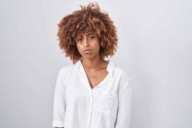 Jovem mulher hispânica com cabelo encaracolado em pé sobre fundo branco cético e nervoso franzindo a testa chateado por causa do problema pessoa negativa
