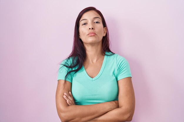 Jovem mulher hispânica em pé sobre fundo rosa cético e expressão de desaprovação nervosa no rosto com pessoa negativa de braços cruzados