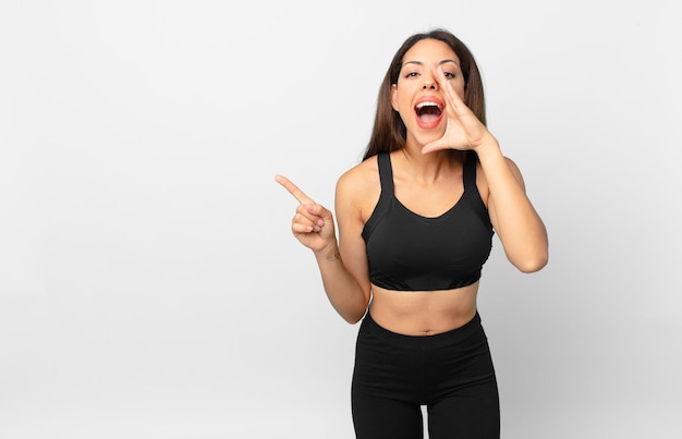 Jovem mulher hispânica se sentindo feliz, dando um grande grito com as mãos ao lado da boca. conceito de fitness