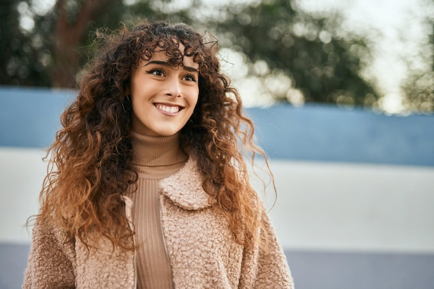 Jovem mulher hispânica sorrindo feliz em pé na cidade