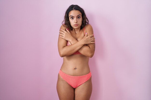 Jovem mulher hispânica vestindo lingerie sobre fundo rosa tremendo e congelando para o frio do inverno com expressão triste e chocada no rosto