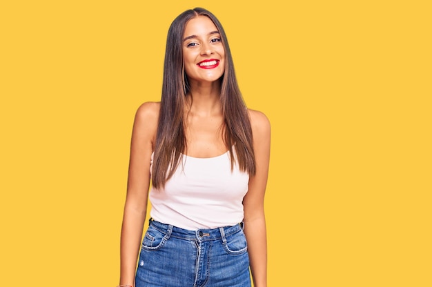 Jovem mulher hispânica vestindo roupas casuais parecendo positiva e feliz em pé e sorrindo com um sorriso confiante mostrando os dentes