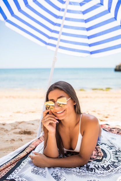 Jovem mulher latina deitada na areia sob o guarda-sol na praia do mar. vocação de verão