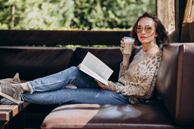 Jovem mulher lendo livro e bebendo café