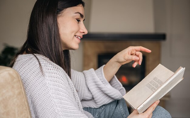 Foto grátis jovem mulher lendo um livro em casa em um fundo de lareira desfocada