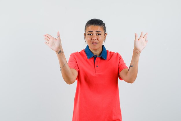 Jovem mulher levantando as mãos em pose de rendição em t-shirt vermelha e está bonita. vista frontal.