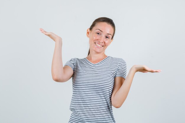 Jovem mulher levantando as palmas das mãos enquanto segurando algo em uma camiseta listrada e parecendo feliz. vista frontal.