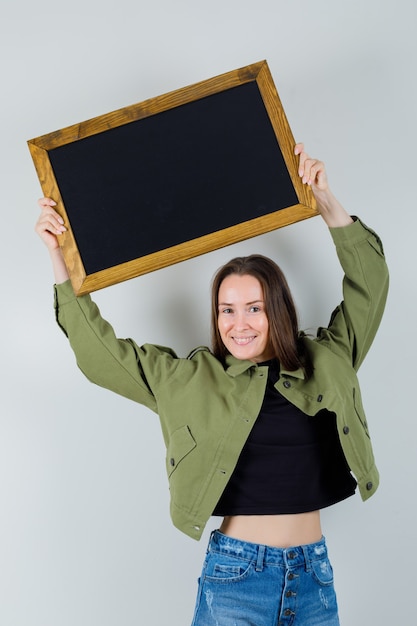 Jovem mulher levantando o quadro aéreo com jaqueta verde, vista frontal.