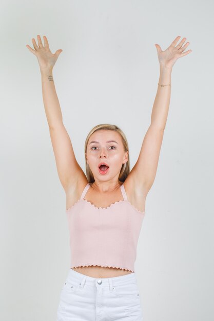 Jovem mulher levantando os braços em camiseta, minissaia e parecendo feliz.