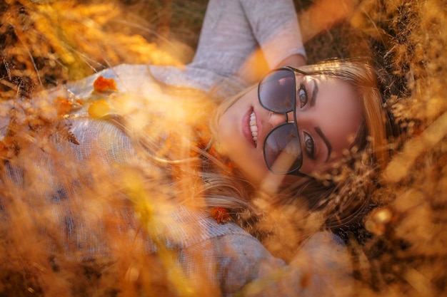 Jovem mulher loira em óculos de sol deitado no capim dourado.