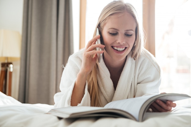 Jovem mulher loira lendo revista e falando no telefone