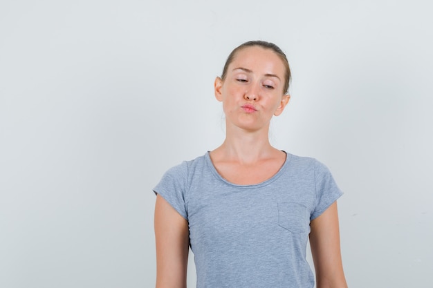 Foto grátis jovem mulher mantendo os lábios dobrados em uma camiseta cinza e olhando pensativa, vista frontal.