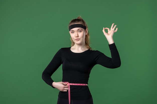 Jovem mulher medindo seu corpo com centímetros sobre fundo verde, vista frontal, atleta, mulher, cor, saúde, corpo, pretas, fit esporte