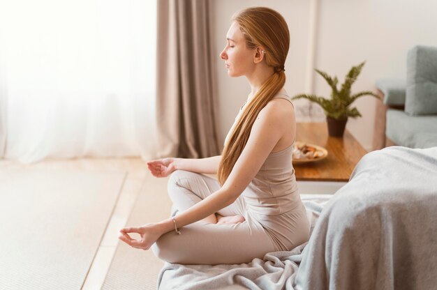 Jovem mulher meditando em casa, vista lateral