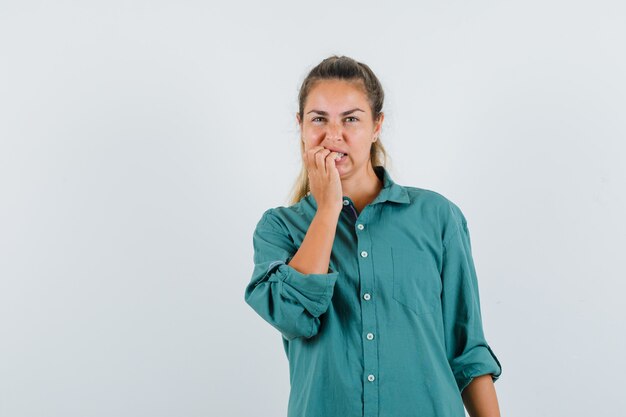 Jovem mulher mordendo os dedos com uma blusa verde e parecendo otimista