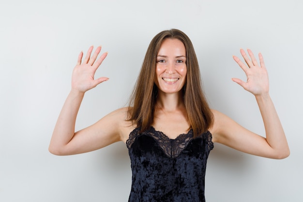 Jovem mulher mostrando as palmas das mãos em uma camiseta preta e parecendo alegre