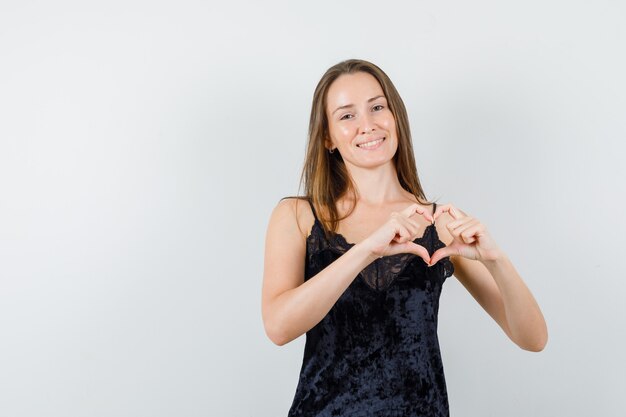 Jovem mulher mostrando gesto de coração em camiseta preta e parecendo alegre