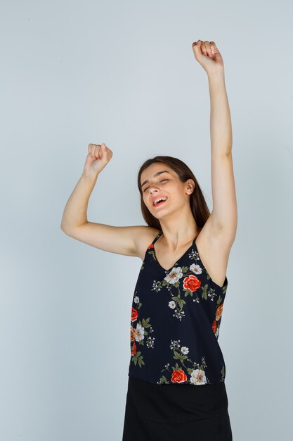 Jovem mulher mostrando o gesto vencedor na blusa, saia e olhando feliz, vista frontal.