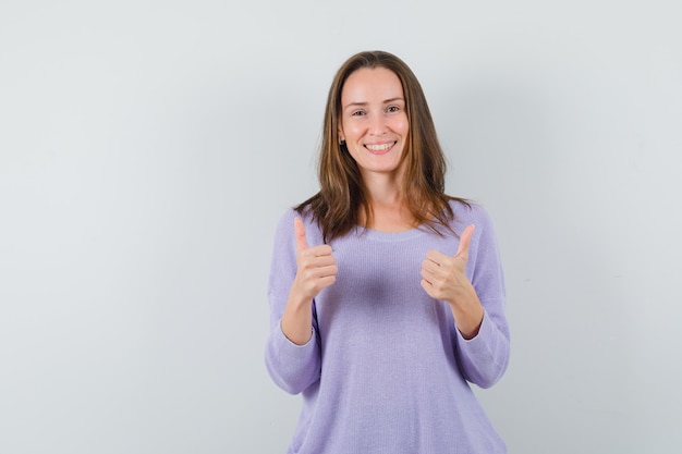 Jovem mulher mostrando o polegar com uma blusa lilás e parecendo feliz