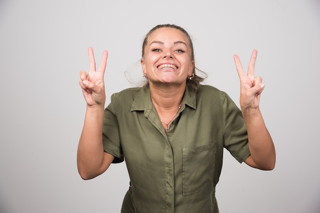 Jovem mulher mostrando os dedos na parede cinza.