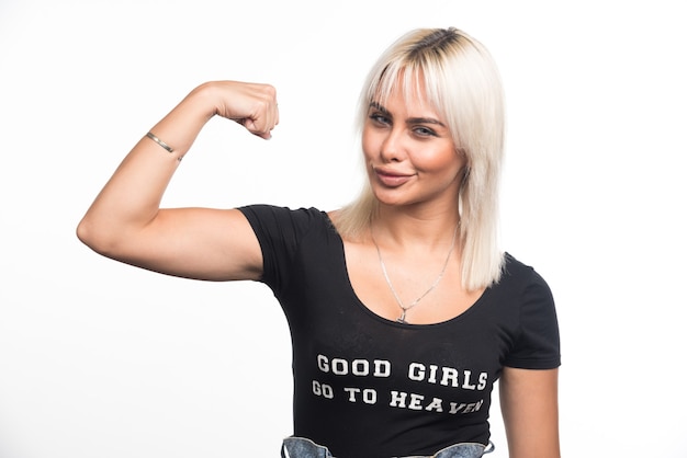 Jovem mulher mostrando os músculos na parede branca com uma expressão feliz.